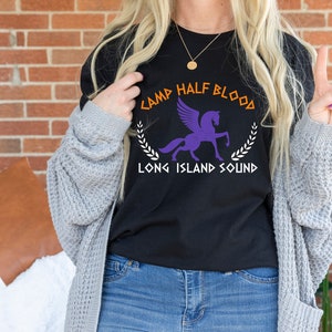 Puede incluir: Camiseta negra con un gr&aacute;fico blanco de un caballo alado y el texto "Camp Half Blood Long Island Sound".