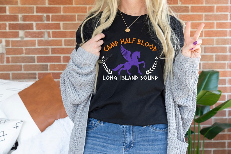 Puede incluir: Camiseta negra con un gr&aacute;fico blanco de un caballo alado y el texto "Camp Half Blood Long Island Sound".