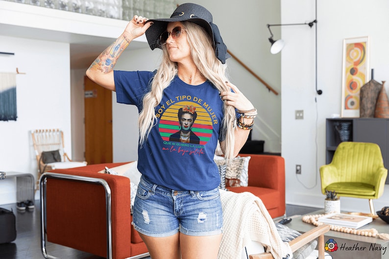 May include: A navy blue t-shirt with a vintage-style graphic of Frida Kahlo. The graphic features a sunset with the text "Soy el tipo de mujer que no necesita la luna para brillar" in Spanish.