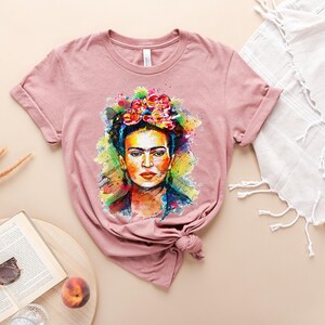 May include: A pink t-shirt with a colorful watercolor portrait of Frida Kahlo wearing a flower crown.