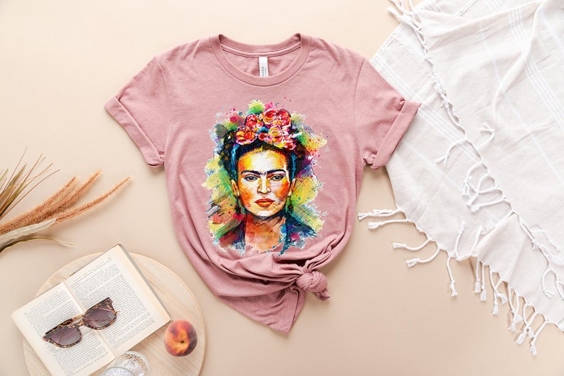 May include: A pink t-shirt with a colorful watercolor portrait of Frida Kahlo wearing a flower crown.