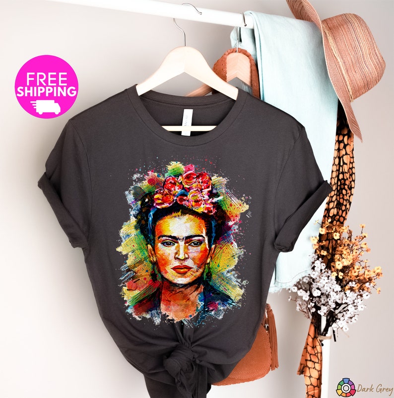 May include: A dark grey t-shirt with a colorful watercolor illustration of Frida Kahlo. The illustration features her signature flower crown and a colorful background.