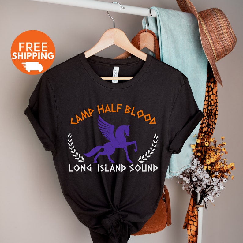 Puede incluir: Camiseta negra con un Pegaso morado y el texto "Camp Half Blood Long Island Sound" en naranja y blanco.
