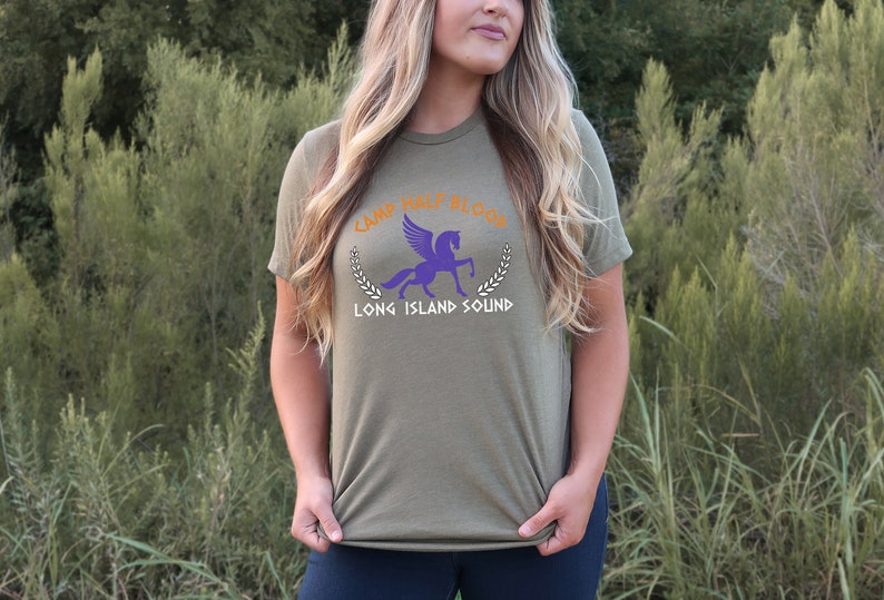 Puede incluir: Una camiseta verde con un pegaso morado y el texto "Camp Half-Blood Long Island Sound" en naranja y blanco.