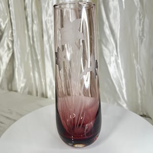 Puede incluir: Un jarrón de vidrio transparente con un diseño floral esmerilado. El jarrón es de color burdeos oscuro y tiene un fondo redondeado.