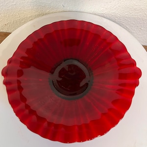 Könnte beinhalten: Eine rote Glasschüssel mit geriffeltem Rand. Die Schüssel besteht aus klarem Glas mit einer roten Tönung. Die Schüssel ist rund und hat einen Durchmesser von etwa 20 cm.