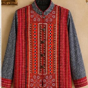 May include: A quilted jacket with a mandarin collar. The jacket features a vibrant red and white central panel with a geometric design, framed by vertical stripes. The sleeves are a contrasting blue with a repeating pattern. The jacket has brown buttons.