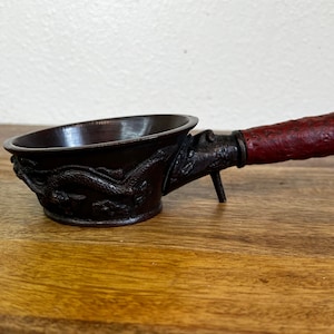 May include: A small, dark brown metal tea caddy with a dragon design and a red wooden handle.