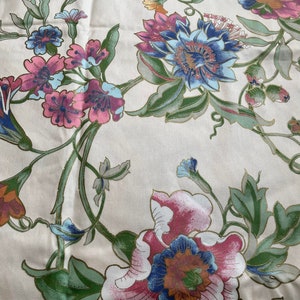 May include: Floral fabric with a cream background. The fabric features large, colorful flowers in shades of pink, blue, and orange, with green leaves and stems. The design has a vintage, botanical feel.