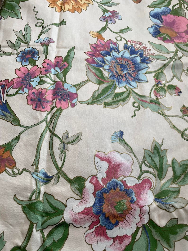 May include: Floral fabric with a cream background. The fabric features large, colorful flowers in shades of pink, blue, and orange, with green leaves and stems. The design has a vintage, botanical feel.