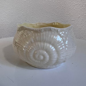 Puede incluir: Un tazón de cerámica blanco con un diseño de concha. El tazón tiene un borde festoneado y un acabado brillante.