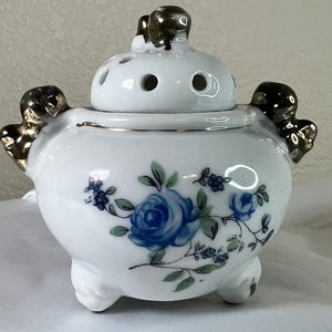 Puede incluir: Quemador de incienso de porcelana blanca con tapa y tres patas. El quemador está decorado con diseños florales azules y verdes y detalles dorados.