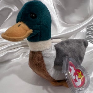 May include: A plush duck toy with a teal head, tan beak, and gray wings. The duck has a white neck and brown body. A red and yellow tag is attached to the duck's wing.