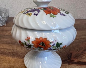 May include: White porcelain candy dish with a swirling design and floral pattern in orange, yellow, green, and purple. The lid has a knob on top.