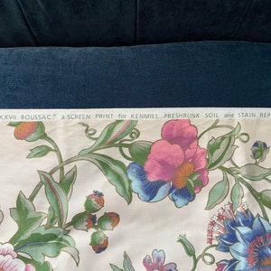May include: Cream-colored fabric with a floral screen print. The design features large pink, blue, and purple flowers with green leaves and stems. Text at the top reads "@MCMLXXXVII BOUSSAC" and "a SCREEN PRINT for KENMILL PRESHRUNK SOIL and STAIN REPELLENT."