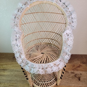 May include: A wicker peacock chair with a white lace trim. The chair is made of natural woven rattan and has a black and white striped base.