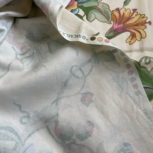 May include: Cream-colored fabric with a floral pattern featuring large, stylized flowers in shades of yellow, pink, blue, and green. The fabric is folded, revealing the underside with a softer, more muted floral design. The text "&copy; MCMLXX" is visible.