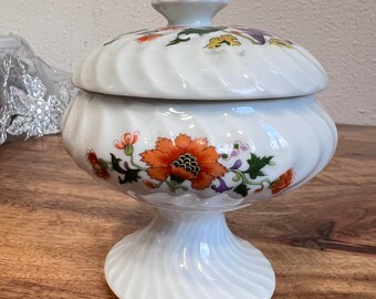 May include: White ceramic candy dish with a lid. The dish has a swirl design and is decorated with orange, yellow, green, and purple flowers.