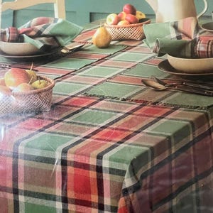 Może przedstawiać: Prostokątny obrus w kratę w odcieniach zieleni, czerwieni, czerni i kremu. Stół jest nakryty plecionymi koszykami z jabłkami i gruszkami, ceramicznymi miskami, złożonymi serwetkami w kratę oraz białym czajnikiem na zielonym tle.
