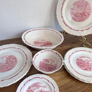 May include: Set of six white ceramic plates with pink floral designs. The plates feature a scalloped edge and a central design of a pink landscape with trees and a house.