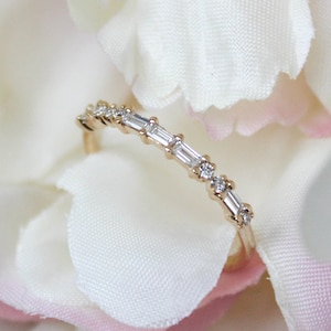 May include: A delicate gold band ring with a row of small, rectangular-shaped diamonds set in a pave setting.