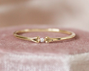 May include: A delicate gold ring with a single small diamond set between two delicate wings.