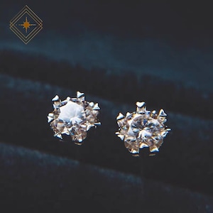 Könnte beinhalten: Ein Paar silberne Ohrstecker mit einem klaren, runden, facettierten Edelstein in der Mitte jedes Ohrsteckers. Die Edelsteine sind von einer silbernen Fassung mit kleinen Punkten umgeben.
