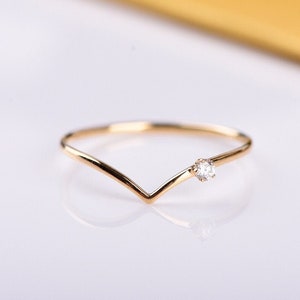 Könnte beinhalten: Ein zarter Goldring mit einem kleinen Diamanten, der in einem V-förmigen Band gefasst ist.