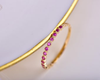 Puede incluir: Un delicado anillo de banda de oro con una fila de pequeñas piedras preciosas de color rosa brillante.