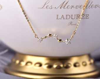 May include: A gold chain necklace with a constellation design featuring small diamonds and stars. The necklace is displayed on a white box with the text "Les Merveilleses LADUREE Paris".