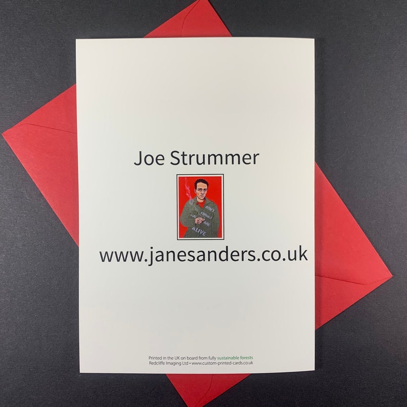 May include: A white card with a red envelope. The card features a black and white illustration of Joe Strummer, a musician, with the text "Don't Forget You're Alive" and the website address "www.janesanders.co.uk".