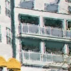 May include: A white building with multiple balconies. The balconies have white railings and are partially obscured by trees.