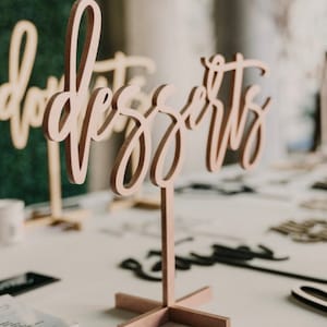 May include: A wooden sign with the word "desserts" written in cursive script. The sign is on a stand with a cross-shaped base.