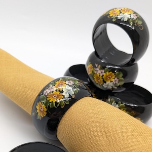 May include: Set of six black wooden napkin rings with hand-painted floral designs in yellow, pink, and white.