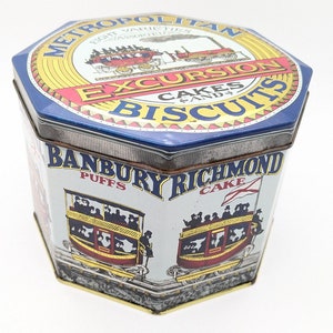 Pode incluir: Uma lata azul e dourada com um rótulo vermelho e branco que diz "Metropolitan Excursion Cakes & Biscuits". A lata tem uma imagem de um trem e o texto "Banbury Richmond Puffs Cake".