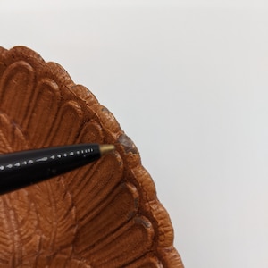 Puede incluir: Un plato de servir de cer&aacute;mica marr&oacute;n en forma de pavo con un dise&ntilde;o detallado de plumas. El plato tiene un borde festoneado y est&aacute; ligeramente astillado en el borde.