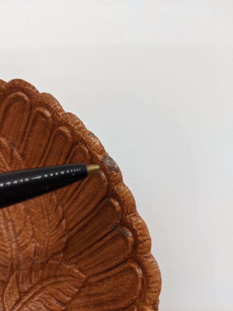 Puede incluir: Un plato de servir de cer&aacute;mica marr&oacute;n en forma de pavo con un dise&ntilde;o detallado de plumas. El plato tiene un borde festoneado y est&aacute; ligeramente astillado en el borde.