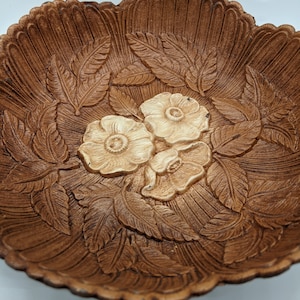 Puede incluir: Un cuenco de madera marr&oacute;n con un dise&ntilde;o tallado de hojas y flores. Las flores son blancas y tienen una textura en relieve.