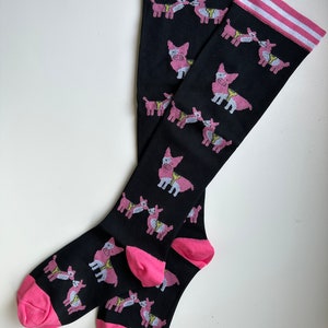 May include: A pair of black knee-high socks with a pink and white stripe at the top. The socks feature a repeating pattern of pink cartoon llamas.