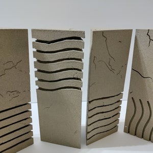 May include: Four beige, rectangular art pieces with carved designs. One features horizontal lines, another wavy lines, and two have crack-like patterns. The pieces are arranged in a row, showcasing a minimalist aesthetic.