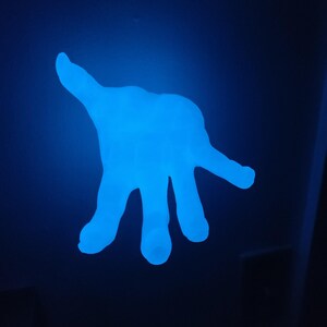 May include: A glowing blue hand-shaped object against a dark blue background. The hand is illuminated, with fingers spread and palm facing the viewer. The object appears to be made of a translucent material.