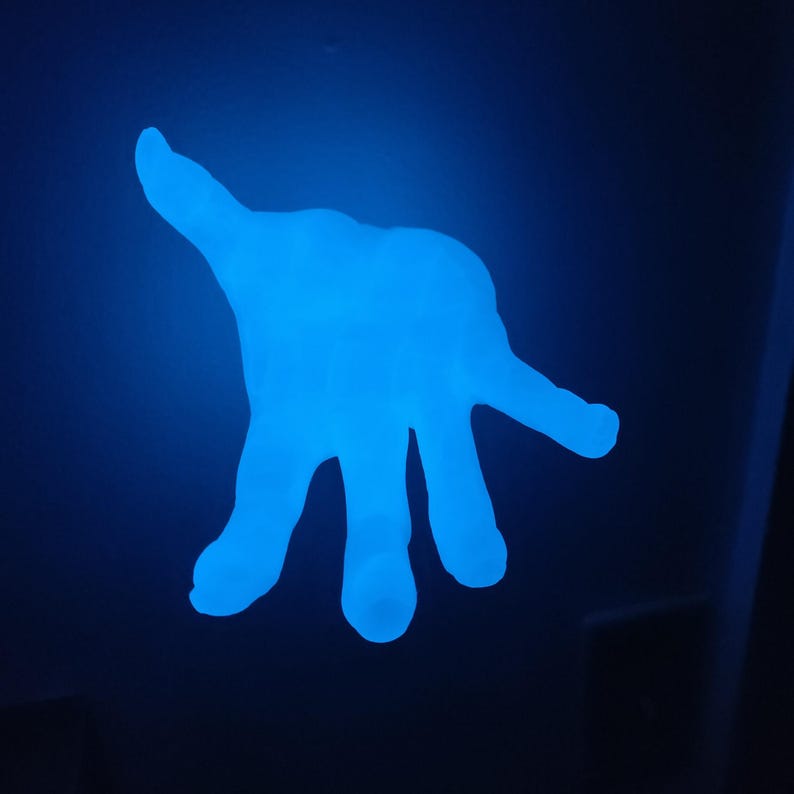 May include: A glowing blue hand-shaped object against a dark blue background. The hand is illuminated, with fingers spread and palm facing the viewer. The object appears to be made of a translucent material.