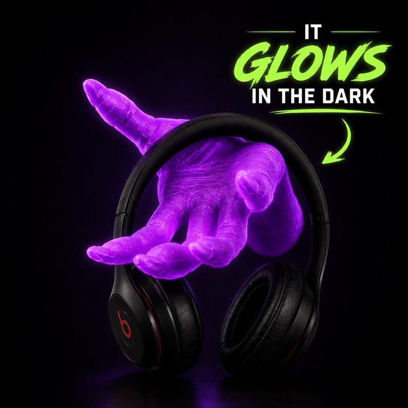 May include: Black headphones with red accents are held by a glowing purple hand against a black background. The text "IT GLOWS IN THE DARK" is displayed in green above the headphones. The headphones have the Beats logo.