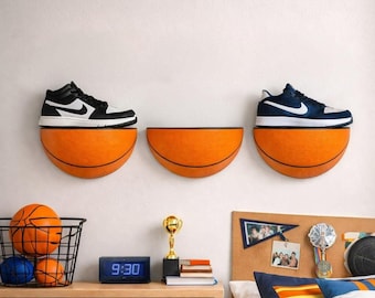 May include: Three orange basketball-shaped wall shelves, with a black and white sneaker on the left shelf and a blue and white sneaker on the right shelf. Below, a wire basket holds two basketballs, a digital clock, and a gold trophy.