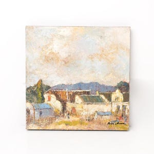 May include: An oil painting on a square canvas depicts a rural landscape with buildings, trees, and mountains under a cloudy sky. The artwork uses a palette of beige, blue, green, and brown tones, with visible brushstrokes. The painting is signed in the lower right corner.