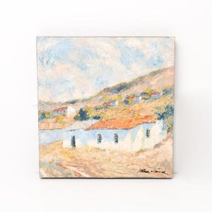 May include: An original oil painting on canvas depicts a rural landscape. The artwork features white buildings with orange roofs nestled against a hillside under a cloudy sky. The painting is signed in the lower right corner.