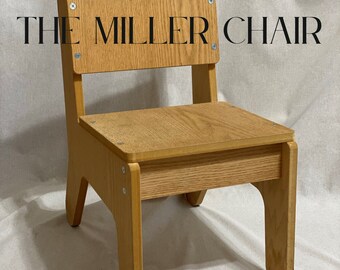 Puede incluir: Una silla de madera con un diseño sencillo. La silla tiene un respaldo y un asiento rectangulares, y las patas están ligeramente curvadas. La silla está hecha de madera marrón claro y tiene un acabado natural. La silla está etiquetada como "THE MILLER CHAIR".