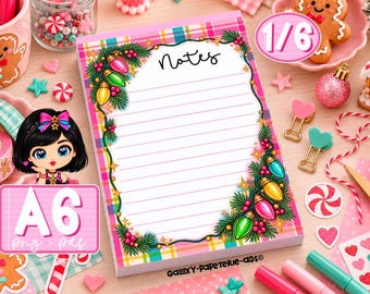 Könnte beinhalten: Ein rechteckiger Notizblock mit linierten Seiten und einem rosa-gelben Karomuster am Rand, verziert mit Tannenzweigen, Stechpalmenbeeren und bunten Weihnachtslichterketten. Oben in der Mitte steht das Wort Notes in schwarzer Schrift.