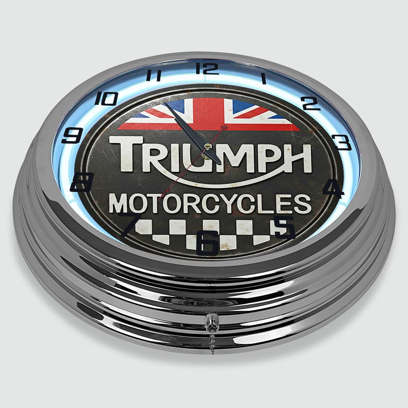 Może przedstawiać: Chromowany zegar ścienny Triumph Motorcycles z niebieskim neonem. Tarcza zegara przedstawia flagę Union Jack i logo Triumph. Zegar ma retro design z szachownicą na dole.