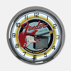 May include: A round wall clock with a chrome bezel. The clock face features the Fender logo, a red electric guitar, and an amplifier. The clock also displays the text "SINCE 1946" and "GUITARS & AMPLIFIERS". The clock has a light blue and yellow neon-style border.